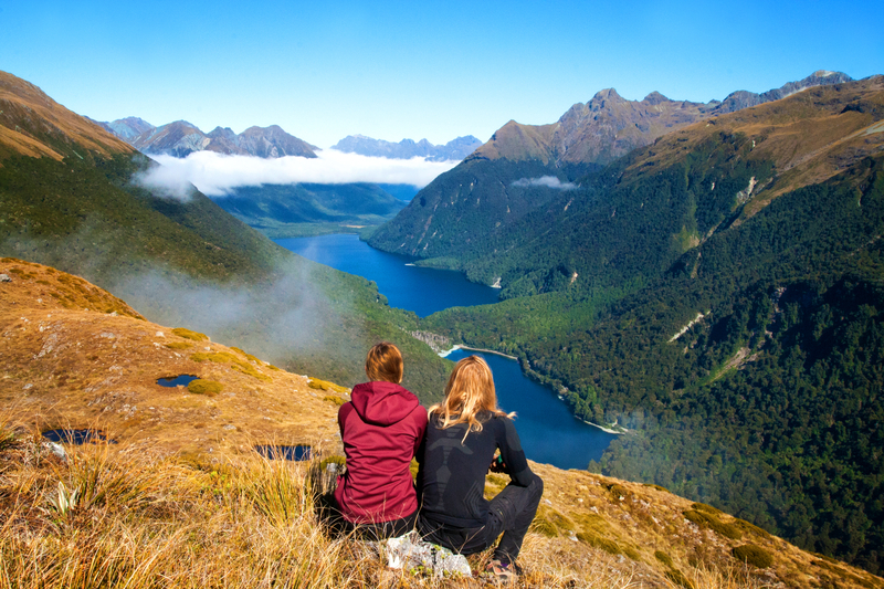 back-view-of-couple-travellers-in-front-of-stunning-mountain-valley-lake-view-key-summit-route-burn-track-fiordland-new-zealand-815442528610